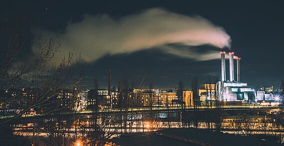Stadt in der Nacht mit rauchenden Fabrikschornsteinen
