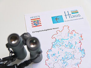 Ein Fernglas und eine Karte der EU-Vogelschutzgebiete in Hessen liegen auf einem Tisch.