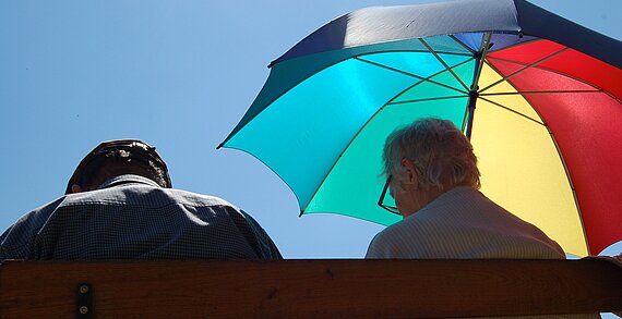 Älteres Paar sitzt mit Sonnenschirm auf einer Bank